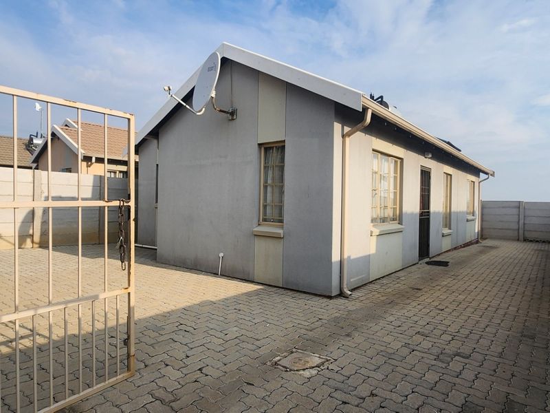 Rear exterior view of the property featuring a paved courtyard, secure metal gate, and precast concrete boundary walls.