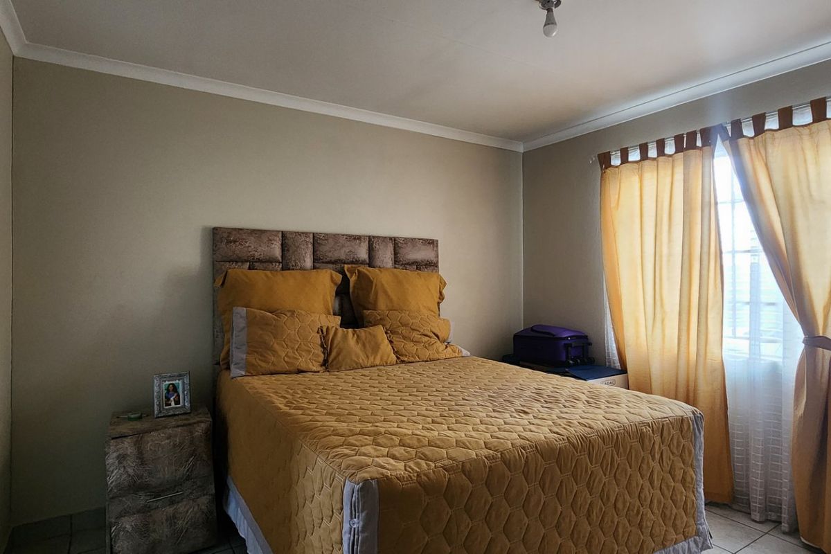 A standard bedroom featuring tiled flooring, coved ceiling details, and a window with curtains, providing a functional and neutral living space.