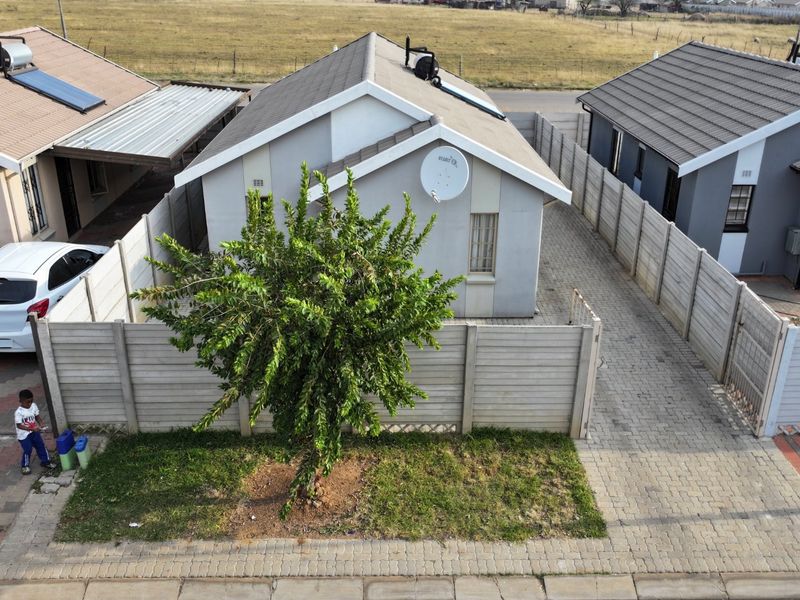 Aerial view of a residential property featuring a tiled roof, solar water heater, satellite dish, and a paved driveway enclosed by precast concrete walls.