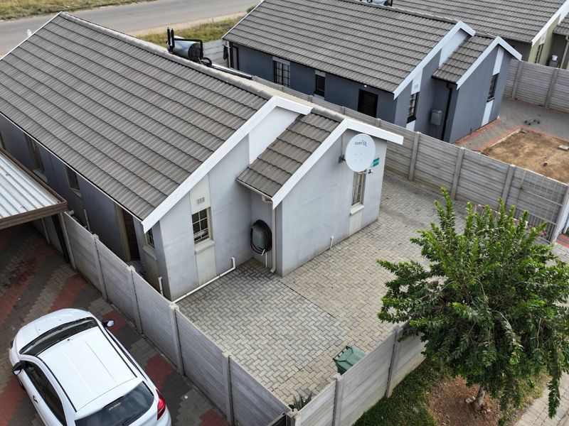 Aerial view of a residential property featuring a tiled roof, paved driveway, and secure precast concrete perimeter walling.