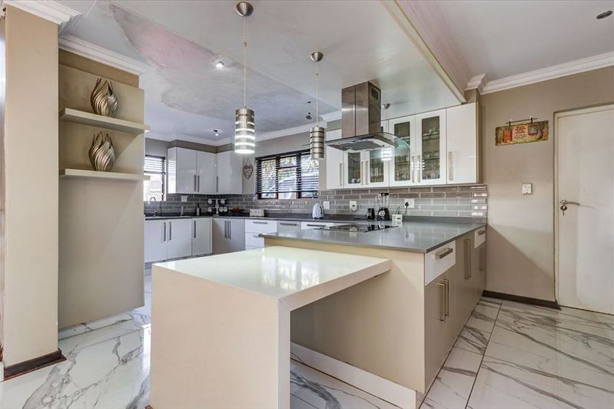 Modern kitchen featuring a central island, stone countertops, subway tile backsplash, and marble-look flooring, with visible ceiling water damage requiring repair.