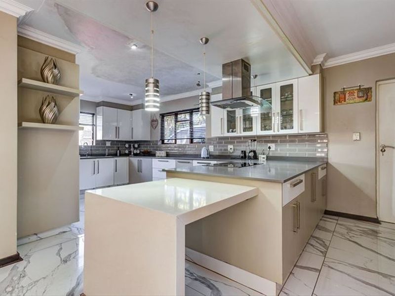 Modern kitchen featuring a central island, stone countertops, subway tile backsplash, and marble-look flooring, with visible ceiling water damage requiring repair.