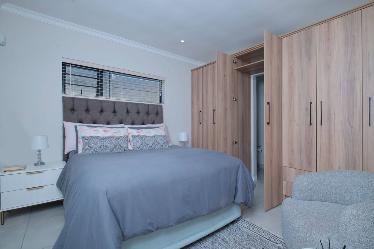 A well-maintained bedroom featuring modern light wood built-in wardrobes, tiled flooring, and recessed ceiling lighting.