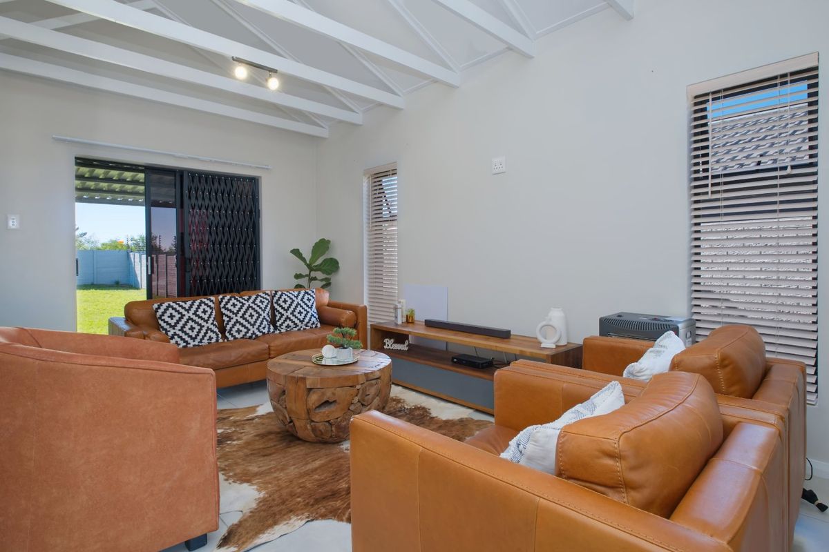 Bright living room featuring exposed white timber rafters, tiled flooring, and large sliding glass doors providing direct access to the rear garden.
