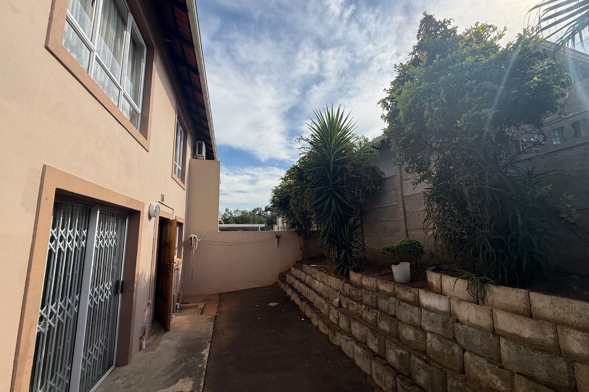 Rear exterior view of the apartment featuring a paved walkway, retaining wall, and secure sliding door access.
