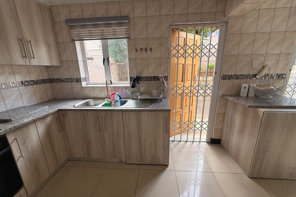 A functional kitchen featuring light wood-look cabinetry, granite countertops, tiled walls, and direct access to the exterior through a security gate.