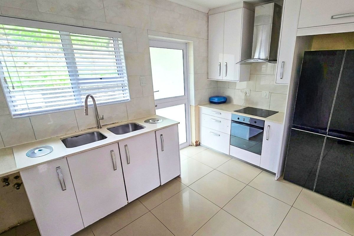 A clean, functional kitchen featuring white cabinetry, integrated appliances including an oven and hob, tiled surfaces, and direct access to the exterior.