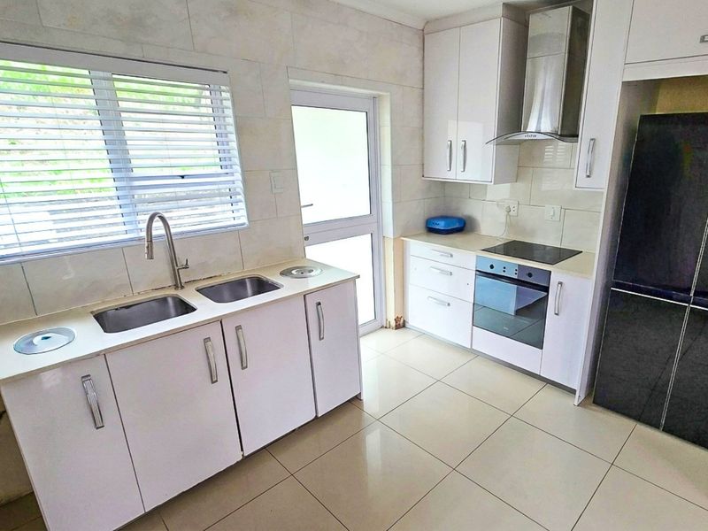 A clean, functional kitchen featuring white cabinetry, integrated appliances including an oven and hob, tiled surfaces, and direct access to the exterior.