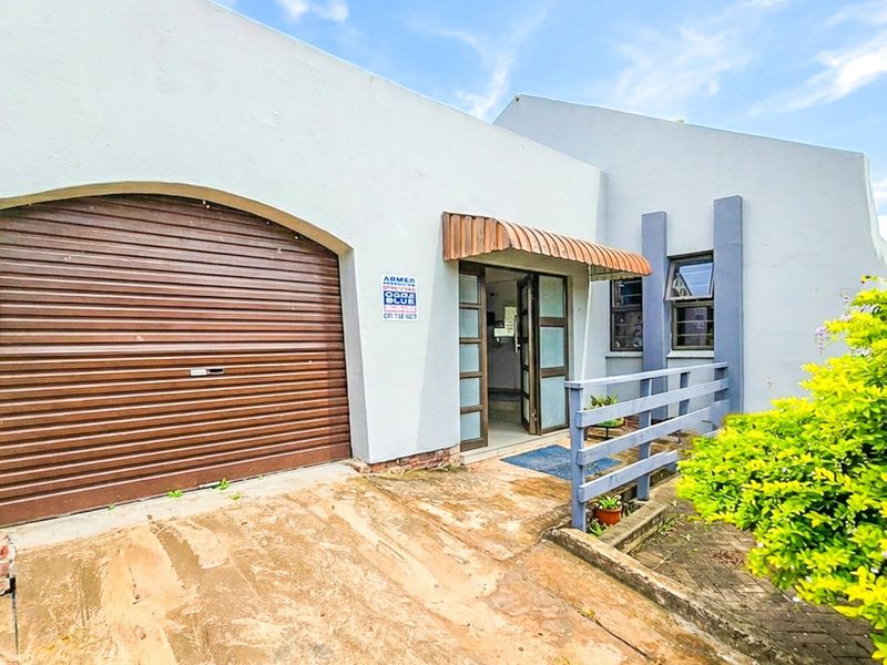Front elevation featuring a roller shutter garage door, covered entrance with an awning, and a paved driveway area.