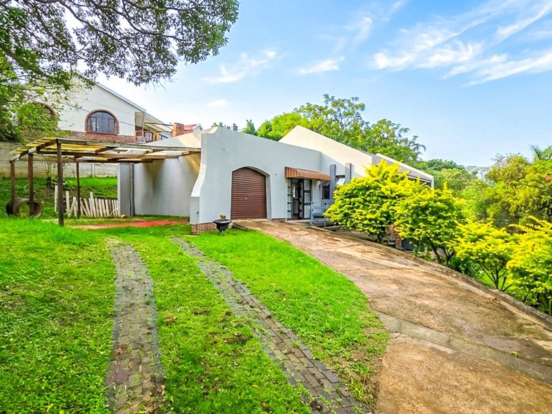 Front view of the property featuring a paved driveway, attached garage, and a covered outdoor area set within a landscaped garden.