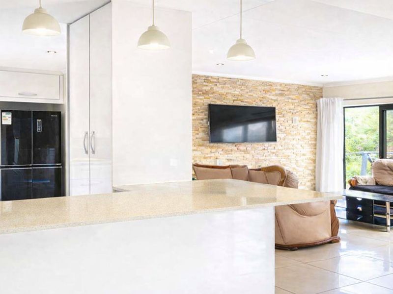 Spacious open-plan living area featuring a modern kitchen with stone countertops, a stone veneer feature wall, and tiled flooring throughout.