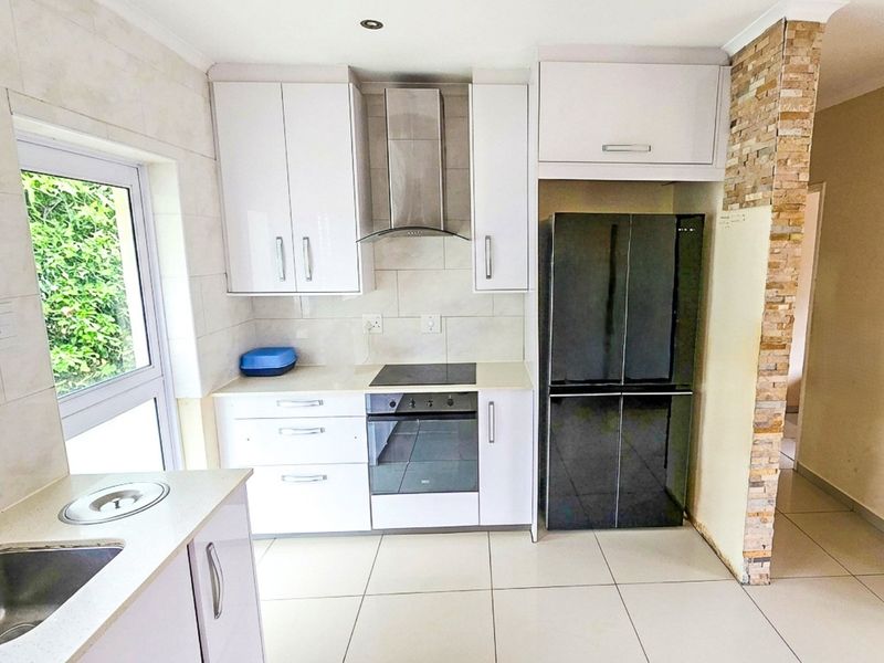 Modern kitchen featuring white cabinetry, integrated stainless steel appliances, stone feature wall, and tiled flooring with ample natural light.