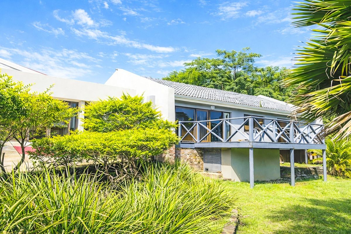 Rear view of the property featuring a raised timber deck, sliding glass doors, and a well-maintained garden setting.