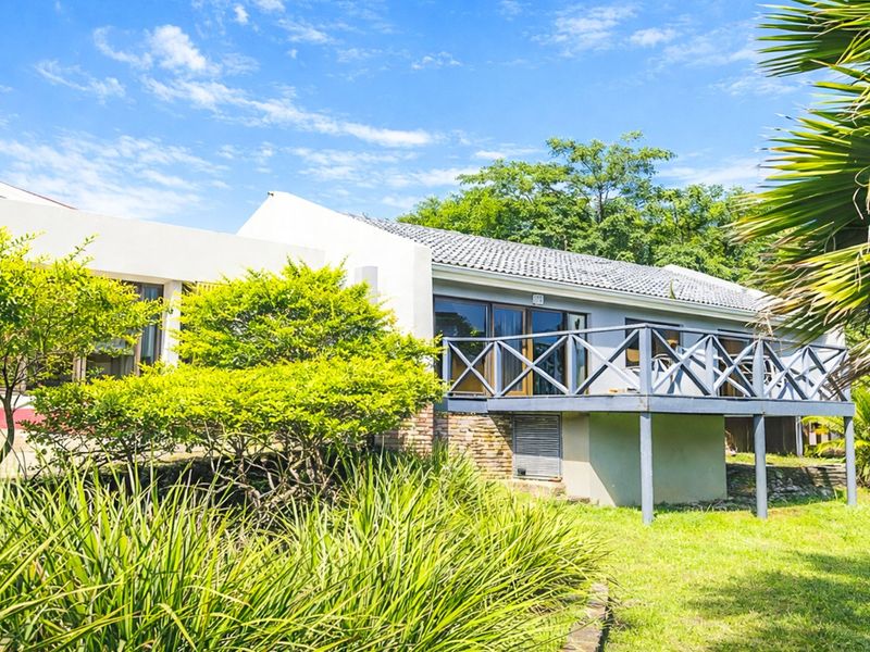 Rear view of the property featuring a raised timber deck, sliding glass doors, and a well-maintained garden setting.