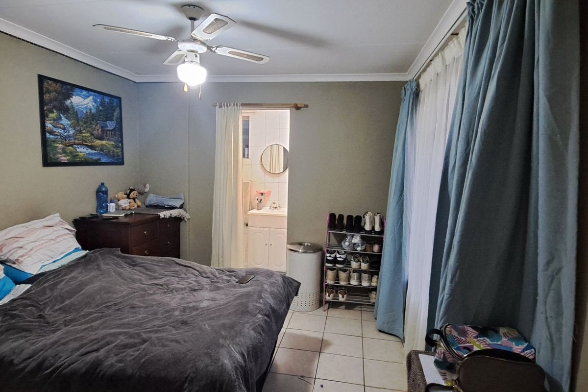 A bedroom featuring tiled flooring, a ceiling fan, and a glass block window, with direct access to an en-suite bathroom.