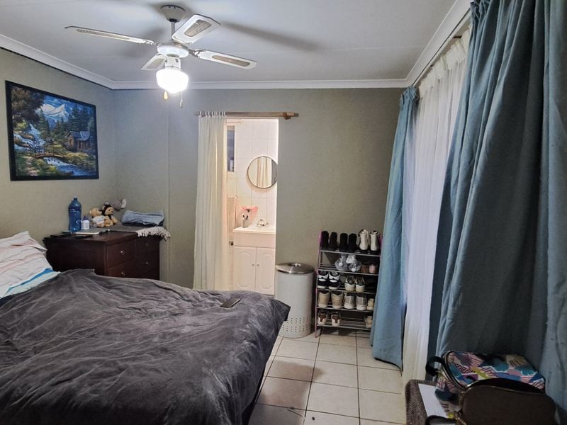 A bedroom featuring tiled flooring, a ceiling fan, and a glass block window, with direct access to an en-suite bathroom.