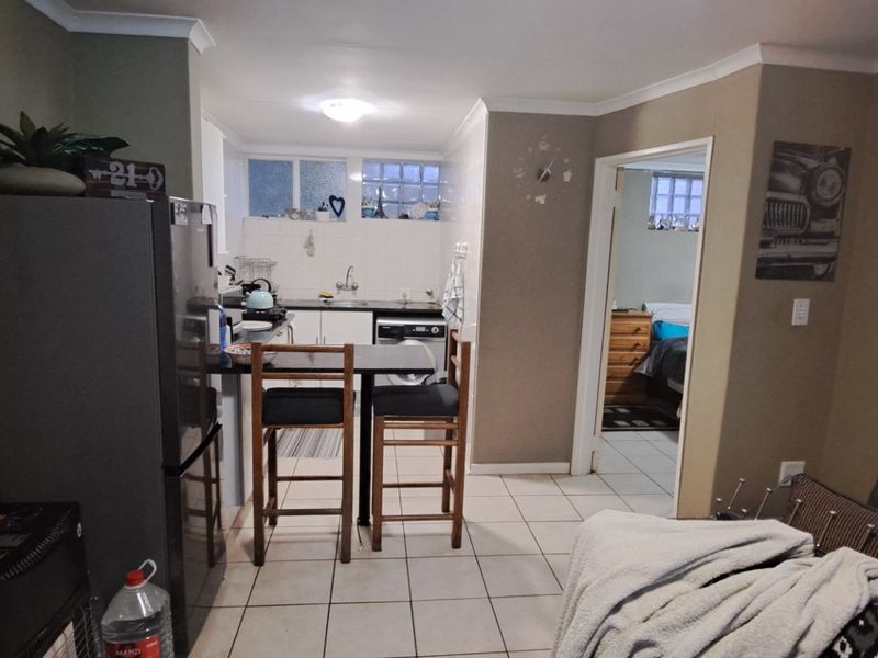 Open plan living area featuring a compact kitchen with breakfast bar, tiled flooring, and direct access to an adjacent bedroom.