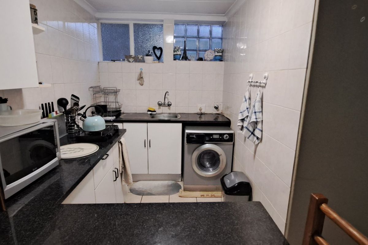 Compact kitchen featuring white cabinetry, dark granite countertops, tiled walls, and a built-in laundry appliance space with glass block window detailing.