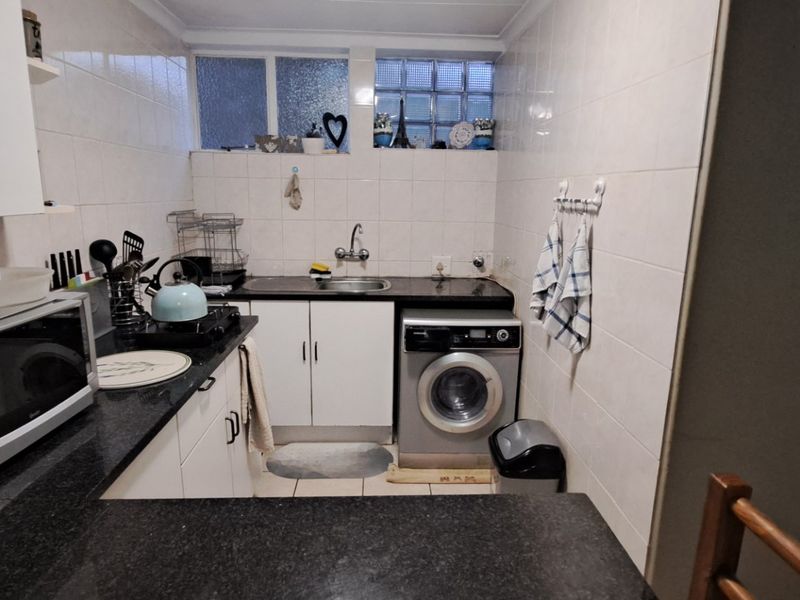 Compact kitchen featuring white cabinetry, dark granite countertops, tiled walls, and a built-in laundry appliance space with glass block window detailing.