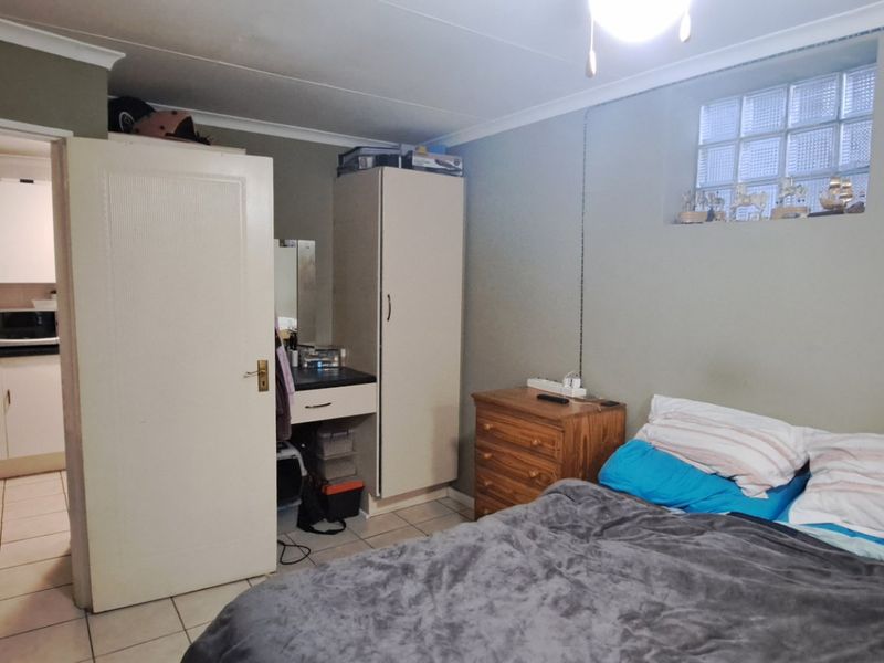 A bedroom featuring tiled flooring, a glass block window, and built-in cabinetry, with an adjacent view into the kitchen area.