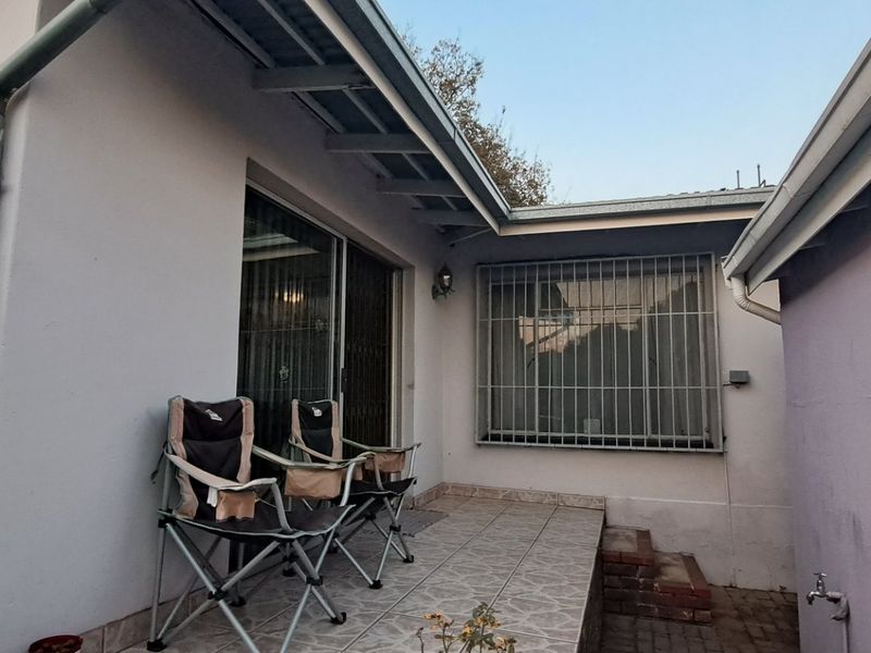 A paved outdoor patio area featuring security bars on windows, a sliding door entrance, and an external water tap.