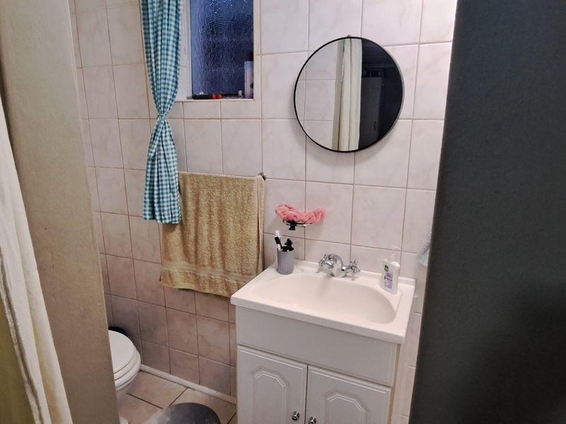 A compact bathroom featuring tiled walls, a vanity cabinet with a basin, and a toilet, with an obscured glass window for privacy.