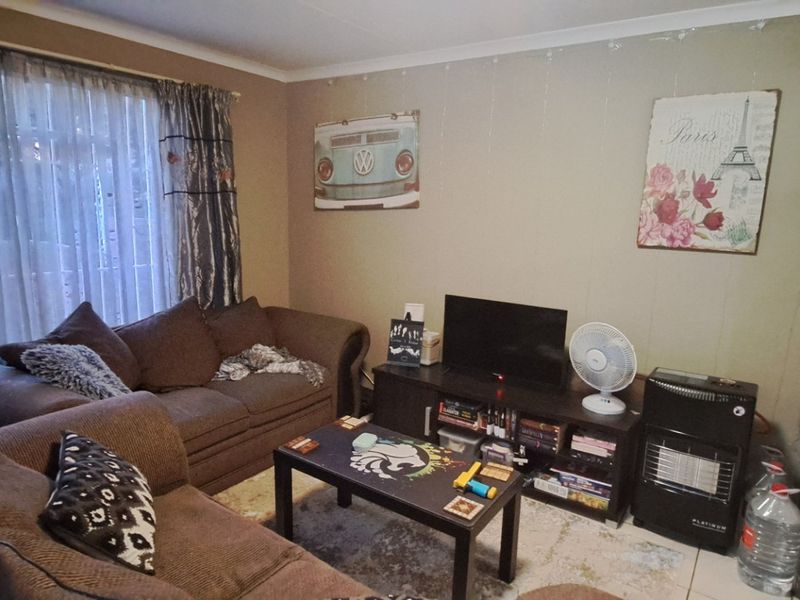 A functional living room area featuring tiled flooring and large window treatments, providing a comfortable space for relaxation.