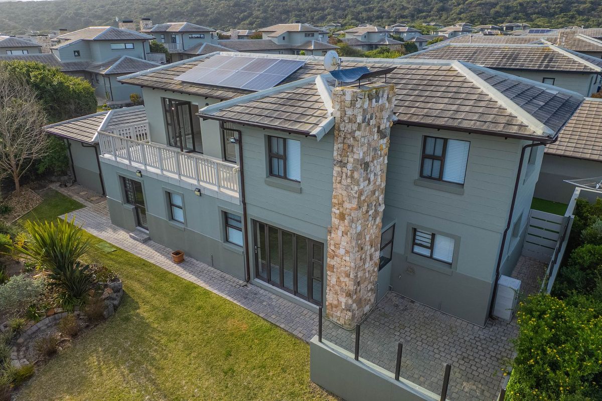 Aerial view of a two-story residential property featuring a stone-clad chimney, solar panels, a paved patio, and a balcony overlooking the garden.