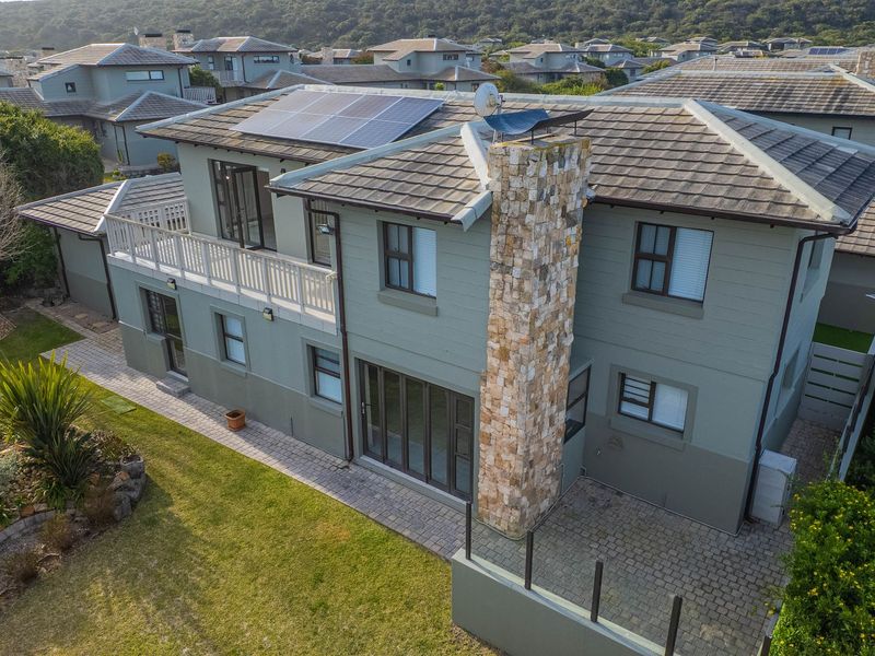 Aerial view of a two-story residential property featuring a stone-clad chimney, solar panels, a paved patio, and a balcony overlooking the garden.