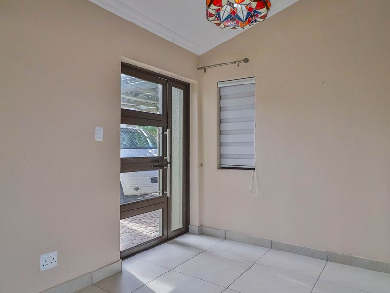 A bright and clean entrance area featuring neutral wall tones, tiled flooring, and a modern aluminium-framed glass door.