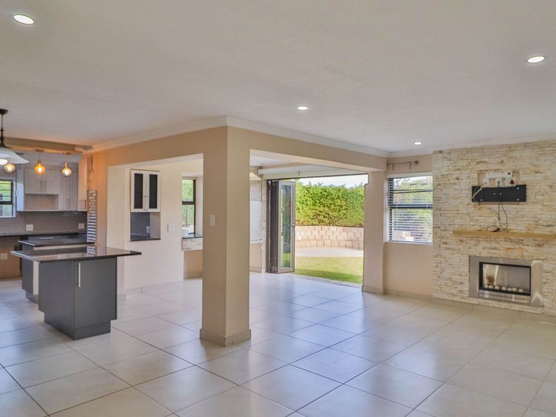 Spacious open-plan living area featuring a modern kitchen with island, stone-clad fireplace, and seamless flow to the outdoor patio through bi-fold doors.