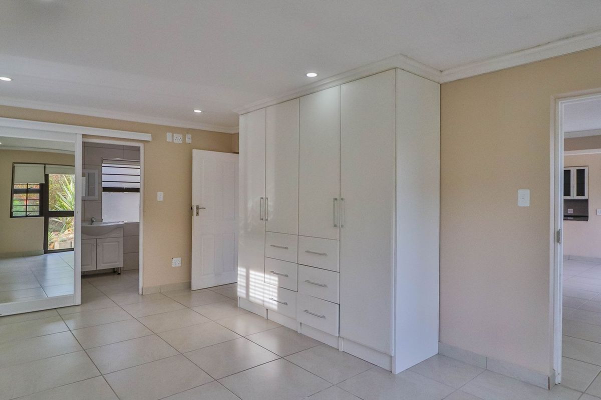 Spacious bedroom featuring neutral tiled flooring, built-in cupboards, and a sliding door leading to an en-suite bathroom.