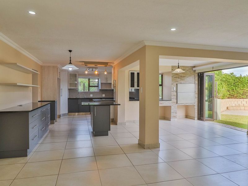 Spacious open-plan kitchen and living area featuring modern cabinetry, stone countertops, tiled floors, and seamless access to the outdoor patio through stacking doors.