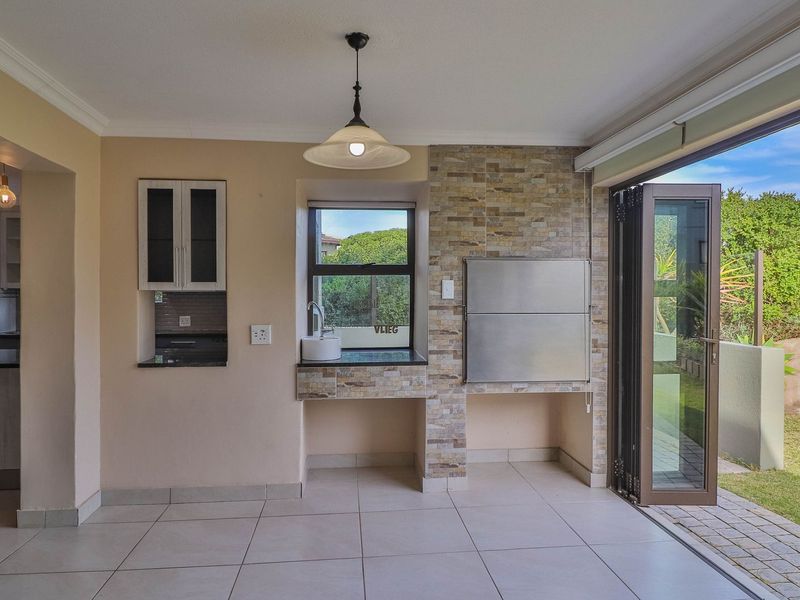 Covered patio area featuring a built-in braai, stone cladding, prep sink with granite countertop, and folding doors opening to the garden.