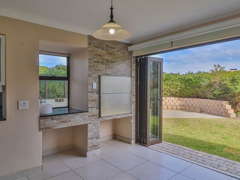 Covered patio area featuring a built-in braai, stone cladding, granite prep area with basin, and folding doors opening to the garden.