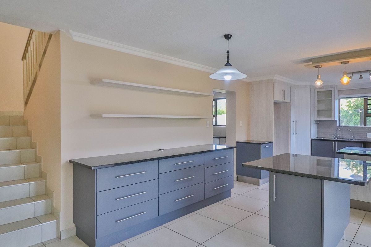 Modern kitchen featuring grey cabinetry, granite countertops, a central island, and tiled flooring, with an adjacent staircase leading to the upper level.