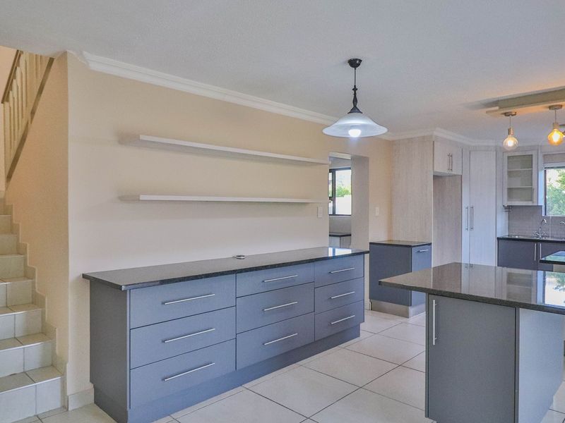 Modern kitchen featuring grey cabinetry, granite countertops, a central island, and tiled flooring, with an adjacent staircase leading to the upper level.