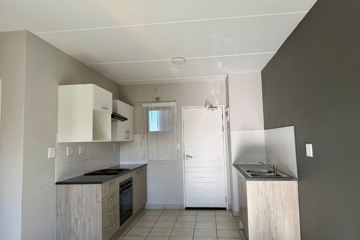 A clean, functional kitchen featuring built-in cabinetry, a hob, oven, extractor fan, and a stainless steel sink with tiled flooring.