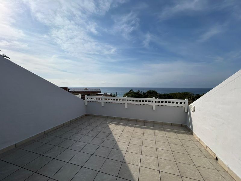A spacious open-air balcony featuring tiled flooring and a decorative white balustrade, offering clear views of the ocean.