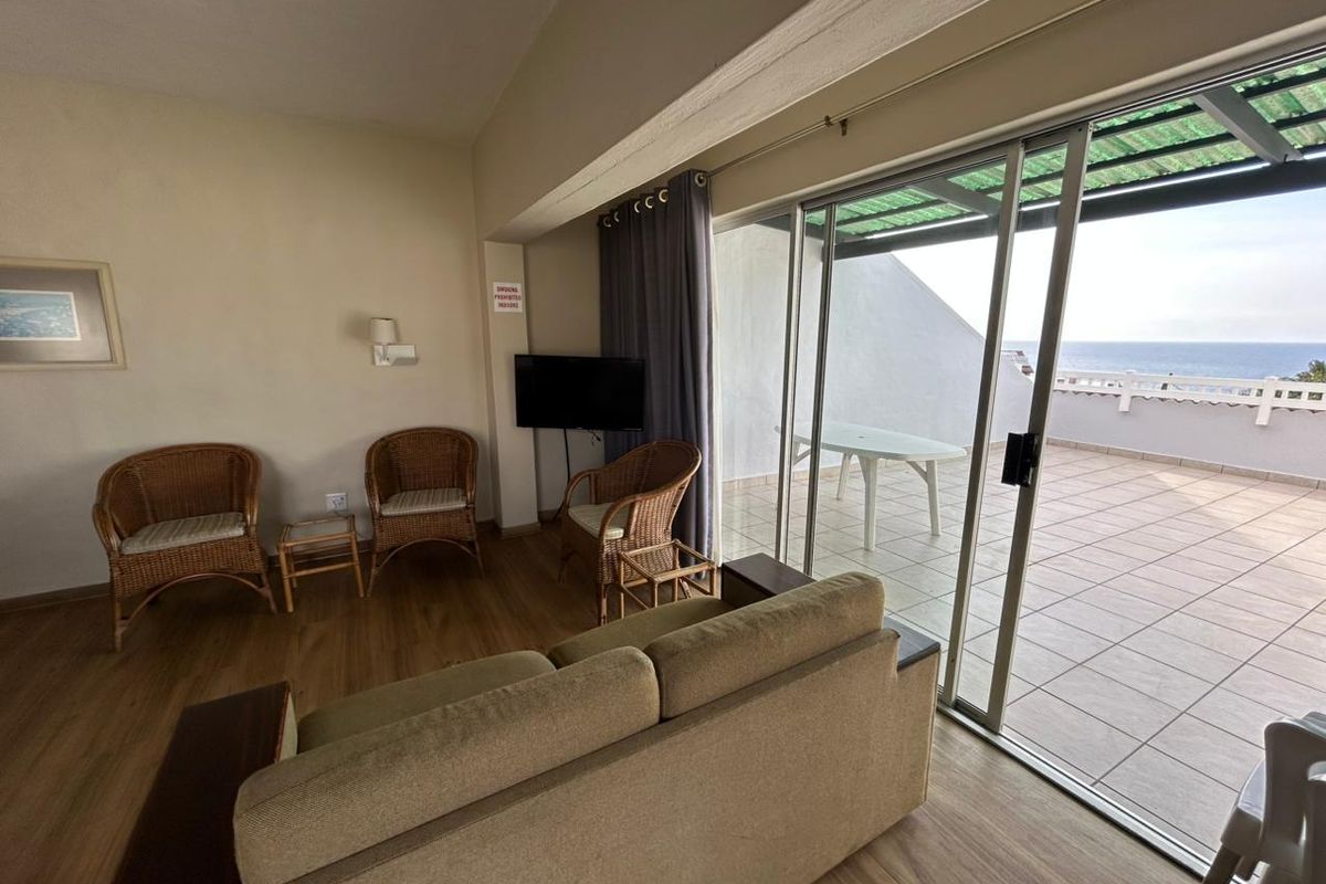 Living room featuring laminate flooring and large sliding glass doors providing direct access to a spacious balcony with ocean views.