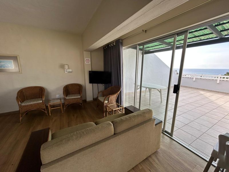 Living room featuring laminate flooring and large sliding glass doors providing direct access to a spacious balcony with ocean views.