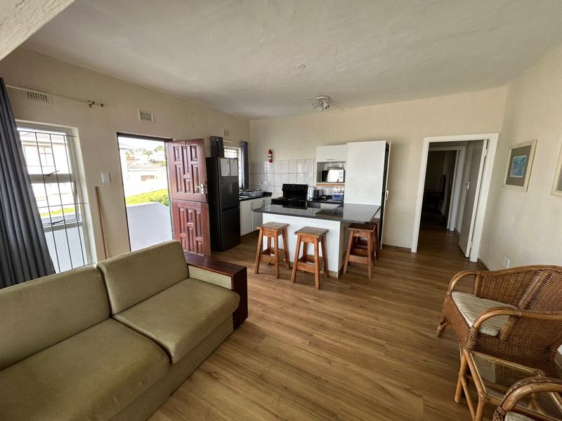 Open-plan living area featuring a compact kitchen with granite countertops, built-in stove, and laminate flooring, leading directly to an exterior entrance.