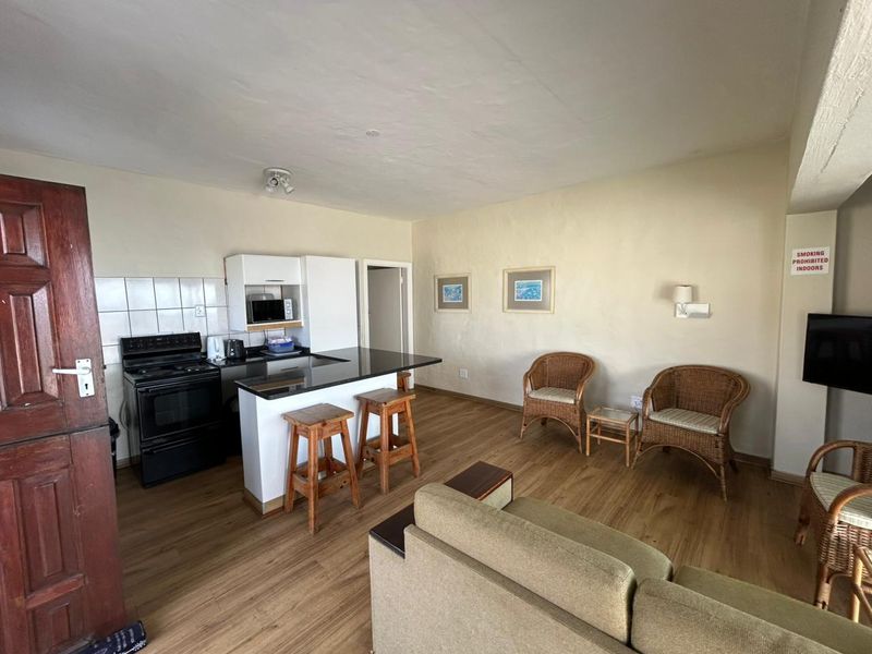 Open-plan living area featuring a compact kitchen with black granite countertops, electric stove, and laminate wood flooring throughout the space.