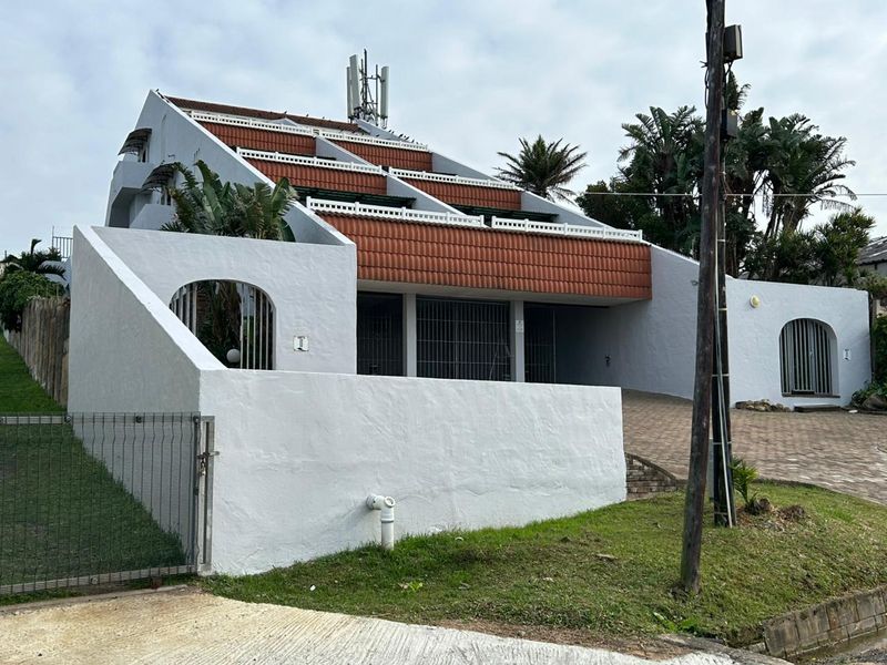 Front elevation of a multi-level apartment complex featuring terracotta roof tiles, a paved driveway, and secure gated access.