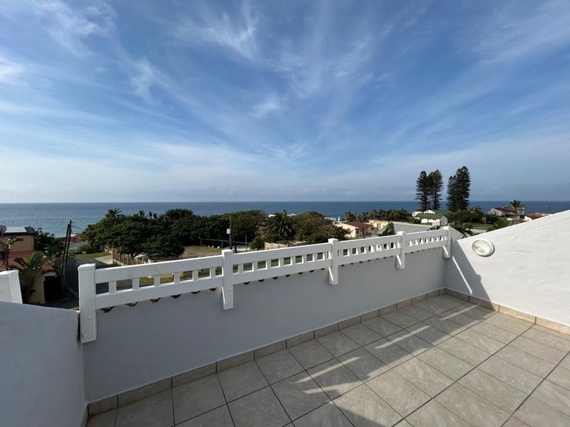 A spacious, open-air balcony featuring tiled flooring and a white balustrade, offering expansive coastal and neighbourhood views.