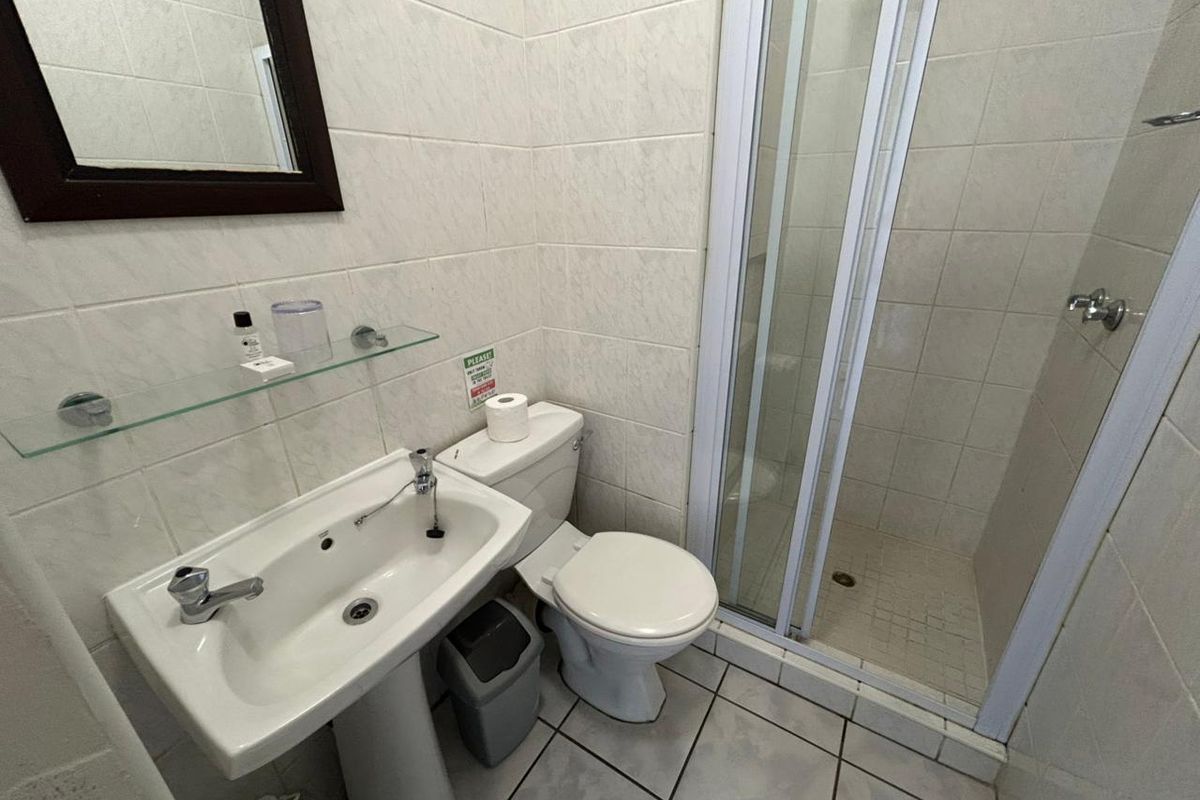 A functional bathroom featuring a pedestal basin, toilet, and a glass-enclosed shower with neutral wall and floor tiling.