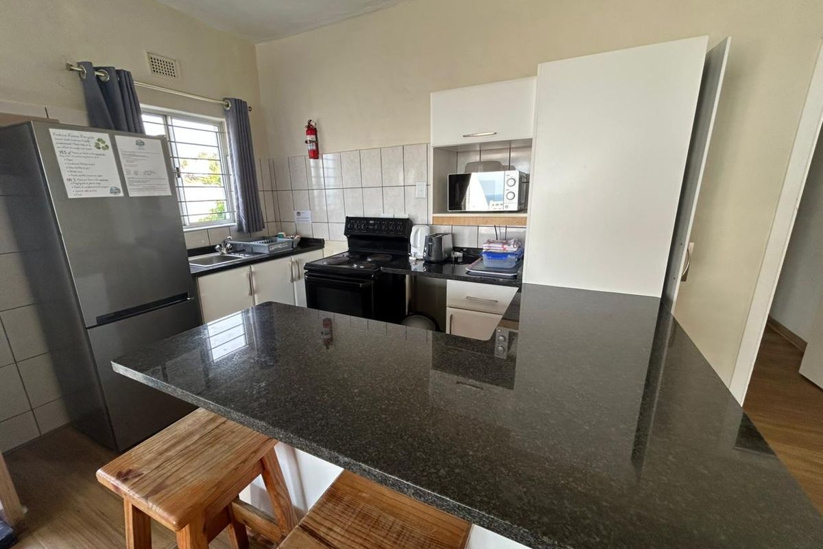 A functional kitchen featuring granite countertops, a breakfast bar, tiled backsplash, and built-in cabinetry with integrated appliance storage.