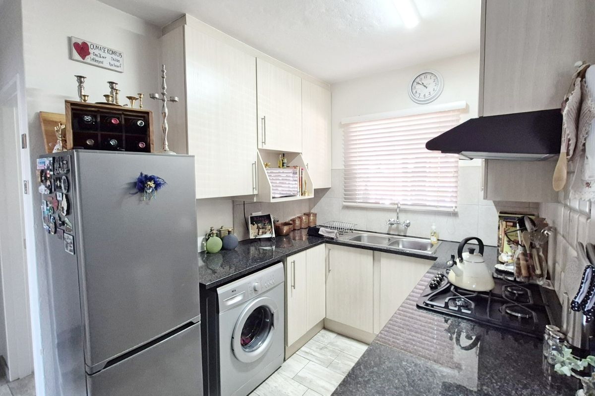 A functional kitchen featuring light-toned cabinetry, granite countertops, a gas hob with extractor fan, and a double basin sink with tiled flooring.