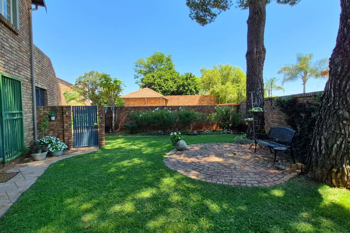 A private rear garden featuring a circular brick-paved patio area, established trees, and a secure brick-walled perimeter.