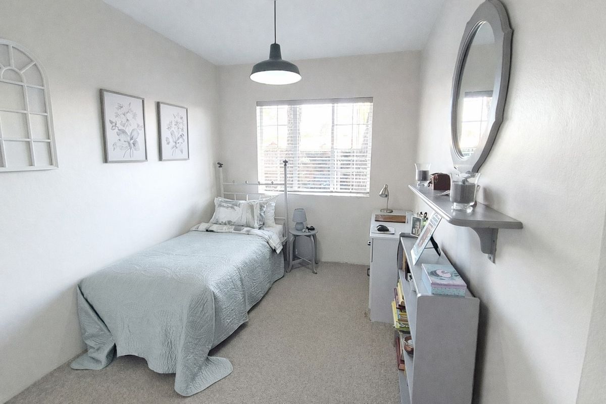 A well-maintained bedroom featuring neutral wall tones, carpet flooring, and a window with fitted blinds, providing a bright and functional living space.